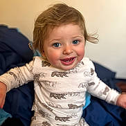 Nathan is registered to the contest to win money with this photo: toddler, child, smiling, blue_eyes, hair, pajamas, animal_print, sitting, indoors, happy, face, person, clothing, soft_light, cute, portrait, baby, cozy, young_child, expression