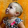 toddler, child, portrait, side_view, blonde_hair, ponytail, dress, pink_bow, orange_background, patterned_clothing, curious, looking_up, young_child, indoor, closeup, cute, happy, baby, skin, face