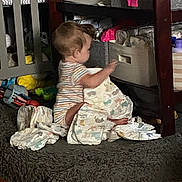 Katharina is registered to the contest to win money with this photo: baby, diaper, rug, toy, storage_bin, nursery, floor, onesie, child, wooden_floor, shelf, clothing, person, indoor, furniture, cute, infant, playtime, colorful, organizer