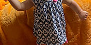 Katharina is registered to the contest to win money with this photo: baby, barefoot, blanket, child, curious_expression, cute, dress, floor, furniture, home, indoor, orange_blanket, patterned_clothing, person, pink_bow, portrait, standing, toddler, wooden_floor, young_child