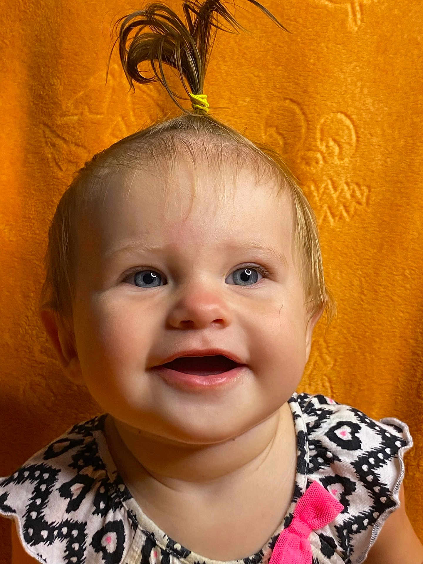 Katharina is registered to the contest to win money with this photo: baby, child, smile, blue_eyes, ponytail, hair_tie, orange_background, patterned_dress, pink_bow, face, portrait, close_up, happy, cute, infant, young_child, indoor, expression, person, toddler