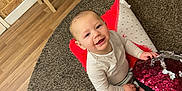Canelo joined the competition — help win amazing prizes! baby, child, smiling, indoors, carpet, cushion, pillow, sequins, flooring, brick_wall, sitting, happy, person, clothing, long_sleeve, pants, cute, head, face, home