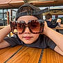 Ayden participe au concours pour gagner de l'argent avec cette photo : child, boy, sunglasses, hat, cap, table, wood, casual, outdoor, cafe, background, person, relaxed, portrait, fashion, cool, young, leisure, daylight, smile