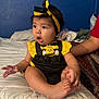 baby, child, infant, bed, clothing, headband, yellow, black, cute, expression, indoor, person, foot, hand, sitting, curious, room, blue_wall, soft_light, holding
