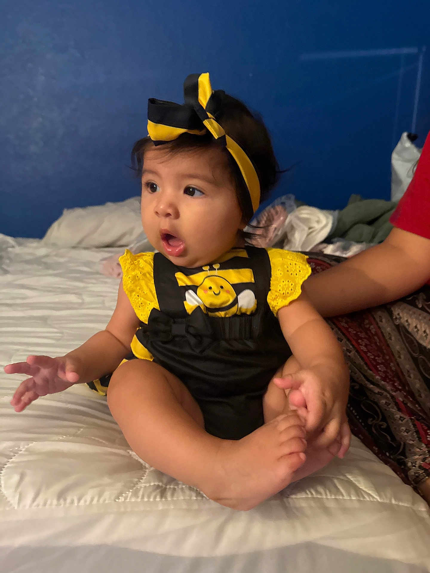 Camila is registered to the contest to win money with this photo: baby, child, infant, bed, clothing, headband, yellow, black, cute, expression, indoor, person, foot, hand, sitting, curious, room, blue_wall, soft_light, holding