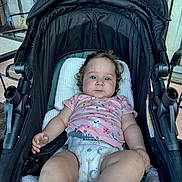 Aylanna joined the competition — help win amazing prizes! baby, black_stroller, casual, child, curly_hair, cute, daylight, diaper, furniture, glass_door, infant, metal_chair, outdoor, patio, person, pink_shirt, relaxed, seated, stroller, young_child