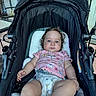 baby, black_stroller, casual, child, curly_hair, cute, daylight, diaper, furniture, glass_door, infant, metal_chair, outdoor, patio, person, pink_shirt, relaxed, seated, stroller, young_child