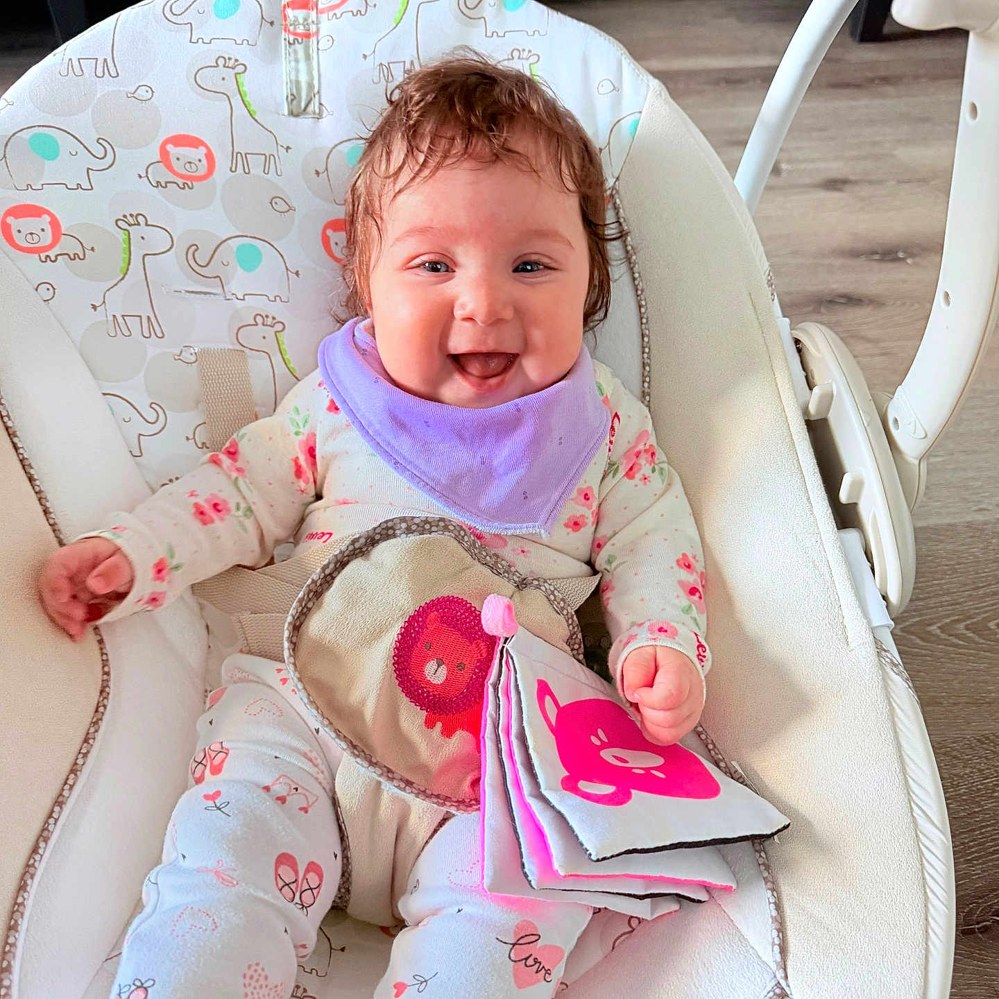 Aylanna is registered to the contest to win money with this photo: animal_print, baby, baby_rocker, child, clothing, comfort, couch, curly_hair, cute, fabric_book, happy, indoor, infant, playful, portrait, purple_bib, seated, smiling, soft_toy, wooden_floor