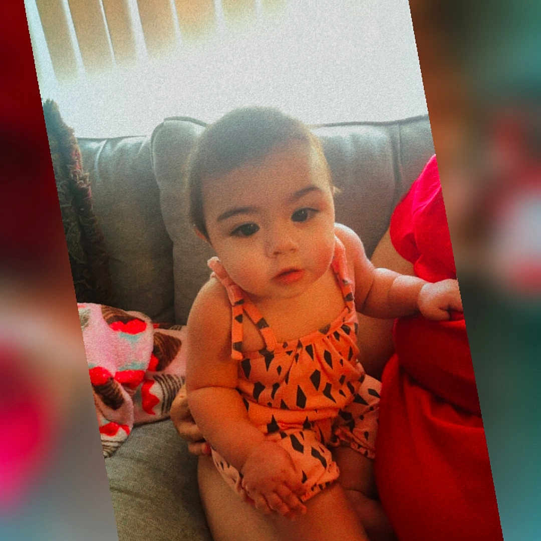 Erinyes joined the competition — help win amazing prizes! adult_arm, baby, blanket, child, clothing, couch, curious, cute, face, home, indoor, infant, lap, patterned, person, portrait, romper, sitting, soft_focus, warm_tones