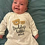 baby, baby_boy, baby_girl, blanket, child, clothing, cute, face, happy, indoors, infant, lying_down, newborn, onesie, portrait, skin, sleepwear, smiling, teddy_bear, text_on_clothing