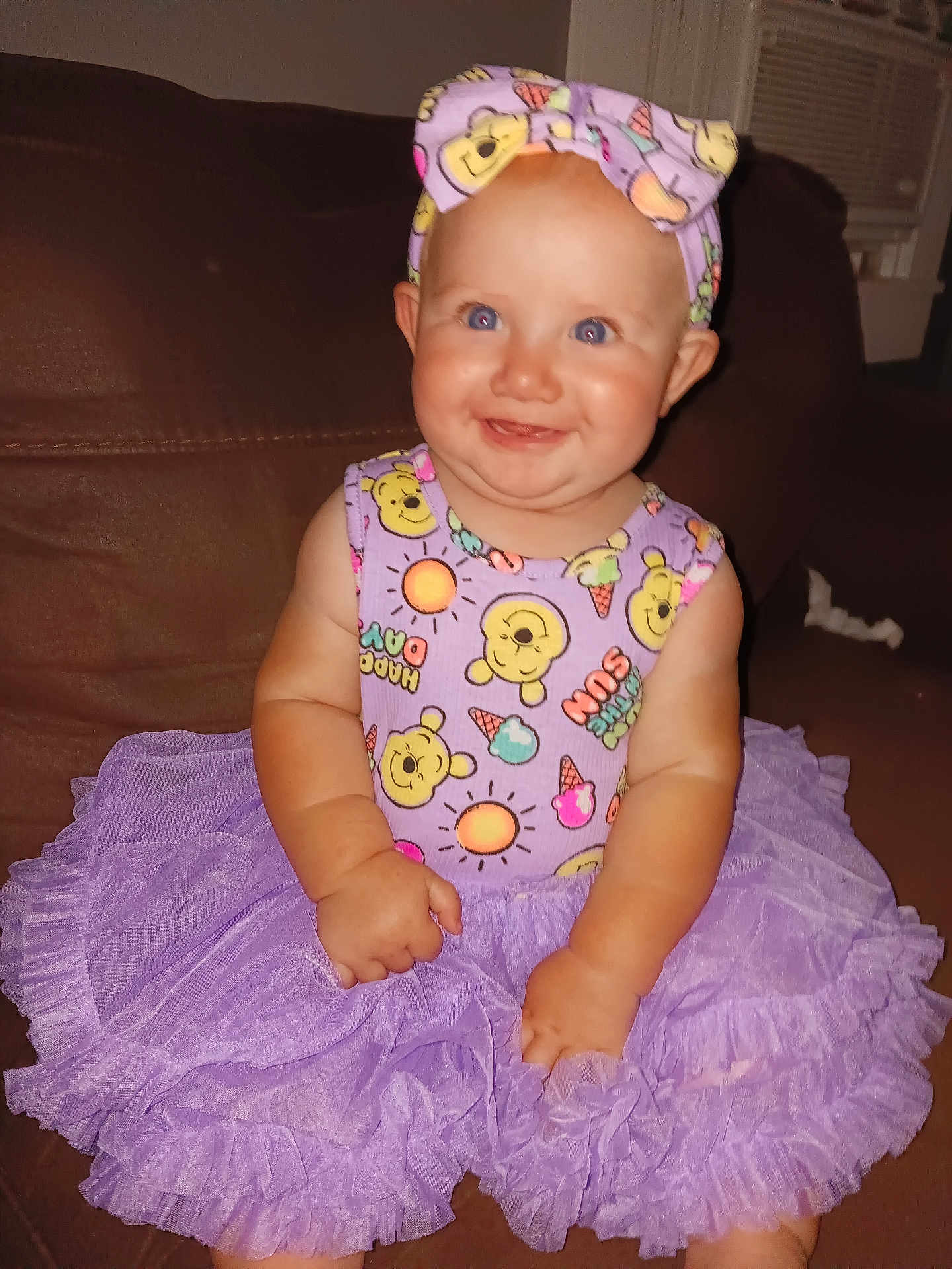 Jasmine joined the competition — help win amazing prizes! baby, tutu, purple, headband, smiling, sitting, couch, indoor, child, happy, clothing, cute, portrait, infant, person, face, playful, cartoon_print, headwear, bright