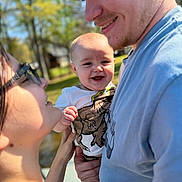 Gunner is registered to the contest to win money with this photo: baby, man, woman, smile, glasses, outdoor, family, holding, happy, portrait, nature, greenery, sunlight, casual_clothing, closeup, people, child, parent, affection, daylight