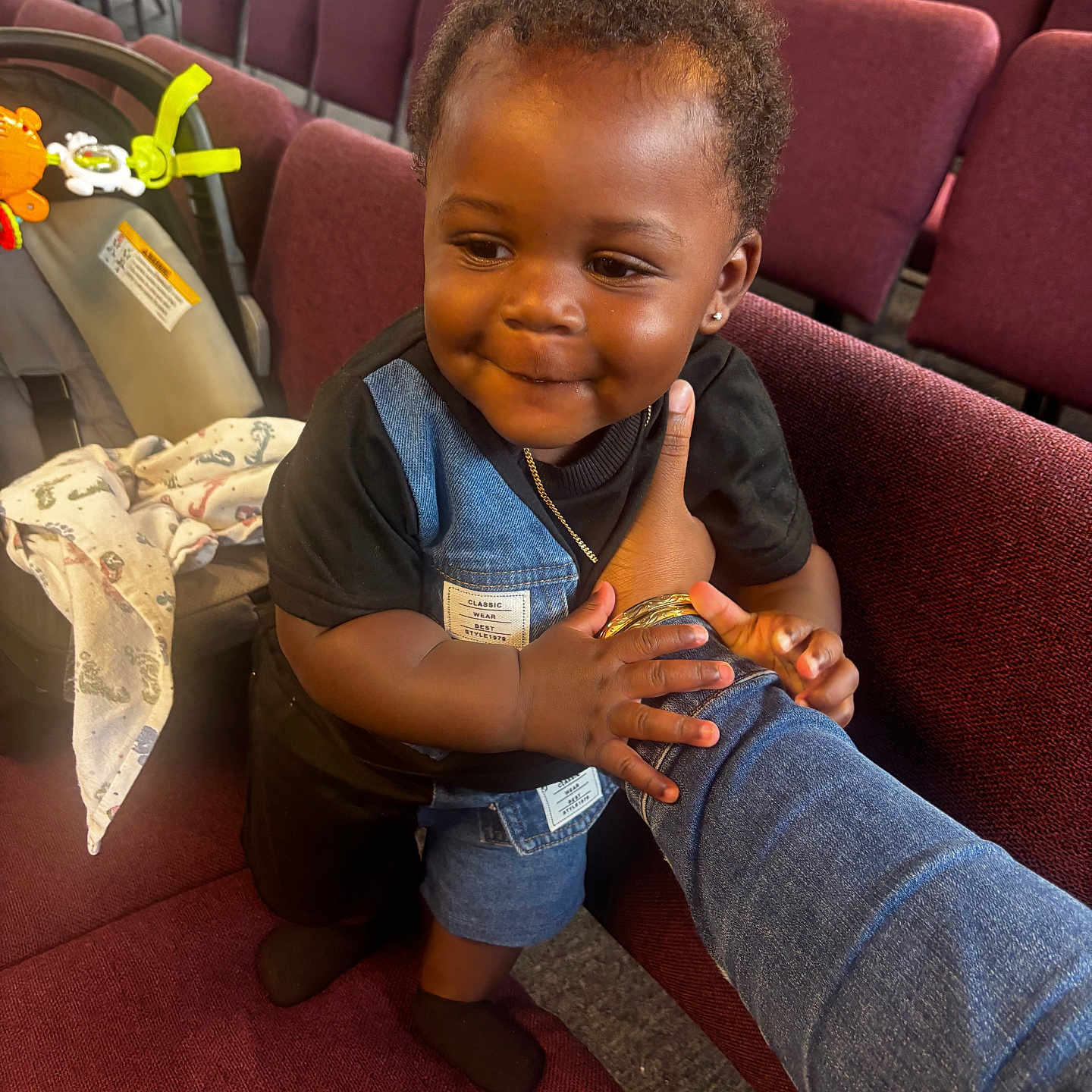 Dezakai joined the competition — help win amazing prizes! toddler, child, smiling, denim, black_shirt, maroon_chair, auditorium, car_seat, toy, baby, holding_arm, earrings, short_hair, indoor, person, cute, portrait, happy, clothing, seat