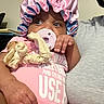 baby, infant, pacifier, pink_bonnet, pink_clothing, soft_toy, adult_arm, indoor, person, cute, child, portrait, closeup, hand, face, expression, holding, comfort, casual, skin