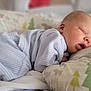 baby, newborn, sleeping, pajamas, striped_clothing, pillow, bed, blanket, soft_fabric, infant, peaceful, cute, face, skin, rest, indoors, child, head, comfort, cozy