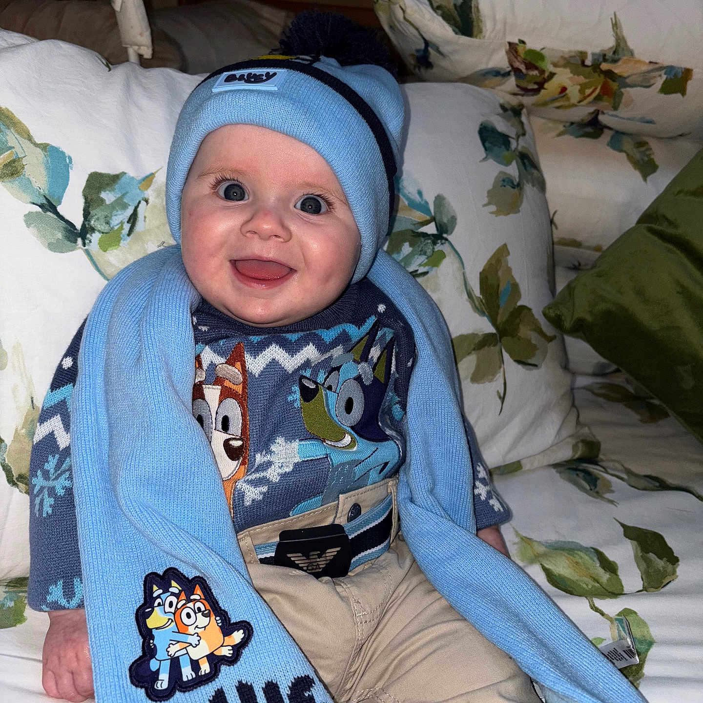 Danny joined the competition — help win amazing prizes! baby, blue, cartoon, child, clothing, couch, cute, floral_pattern, happy, hat, indoor, infant, person, pillow, portrait, scarf, seated, smile, sweater, warm