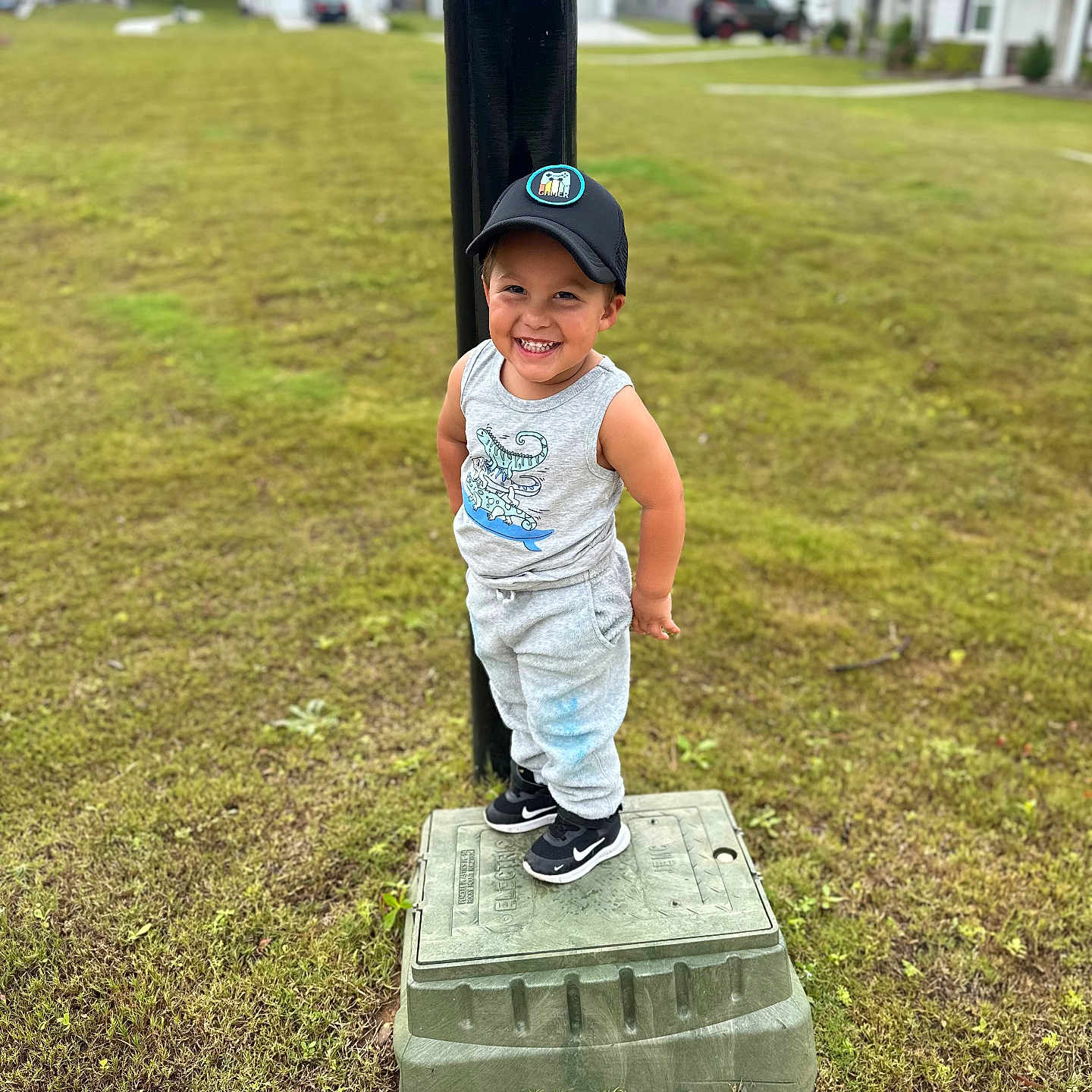 Arthur joined the competition — help win amazing prizes! cap, casual_clothing, child, daylight, grass, greenery, happy, house, nature, outdoor, person, playful, portrait, smiling, sneakers, standing, suburb, tank_top, toddler, utility_box