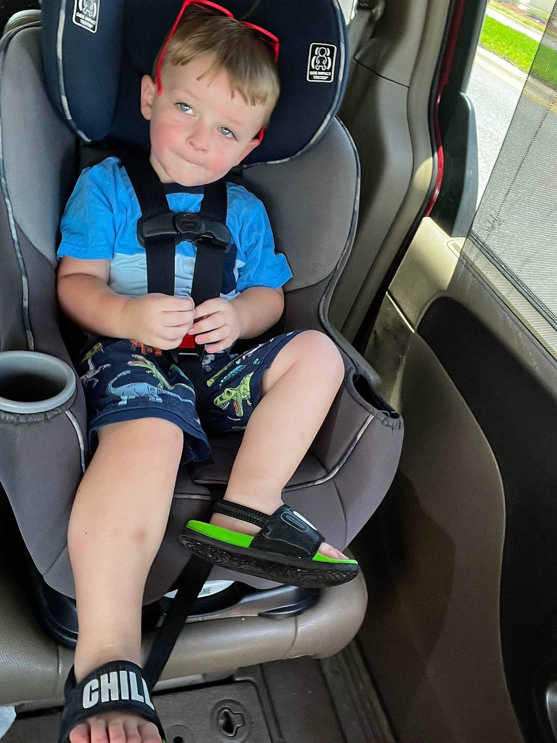William is registered to the contest to win money with this photo: auto_part, automotive_design, automotive_exterior, car, car_seat, car_seat_cover, comfort, leg, mode_of_transport, motor_vehicle, person, product, shorts, smile, sneakers, steering_part, steering_wheel, toddler, vehicle, vehicle_door
