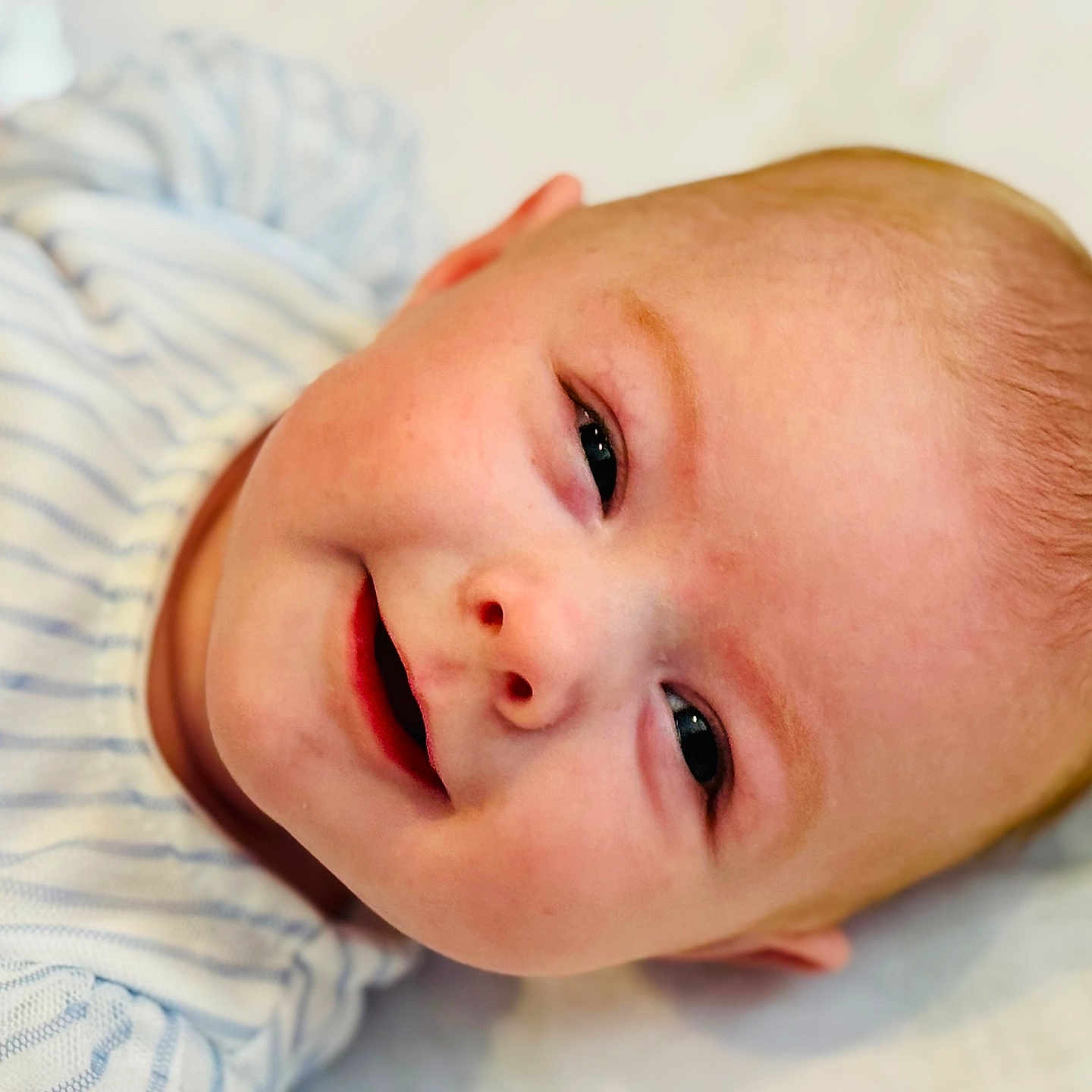 Ensley is registered to the contest to win money with this photo: baby, child, closeup, cute, expression, eyes, face, happy, head, human, infant, lying_down, mouth, newborn, portrait, skin, smiling, soft_surface, striped_clothing, young