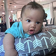 Kai is registered to the contest to win money with this photo: baby, infant, child, blue_shirt, pillow, patterned_pillow, indoor, living_room, furniture, curious, wide_eyes, tongue_out, cute, person, portrait, soft_lighting, home, decor, table, chair
