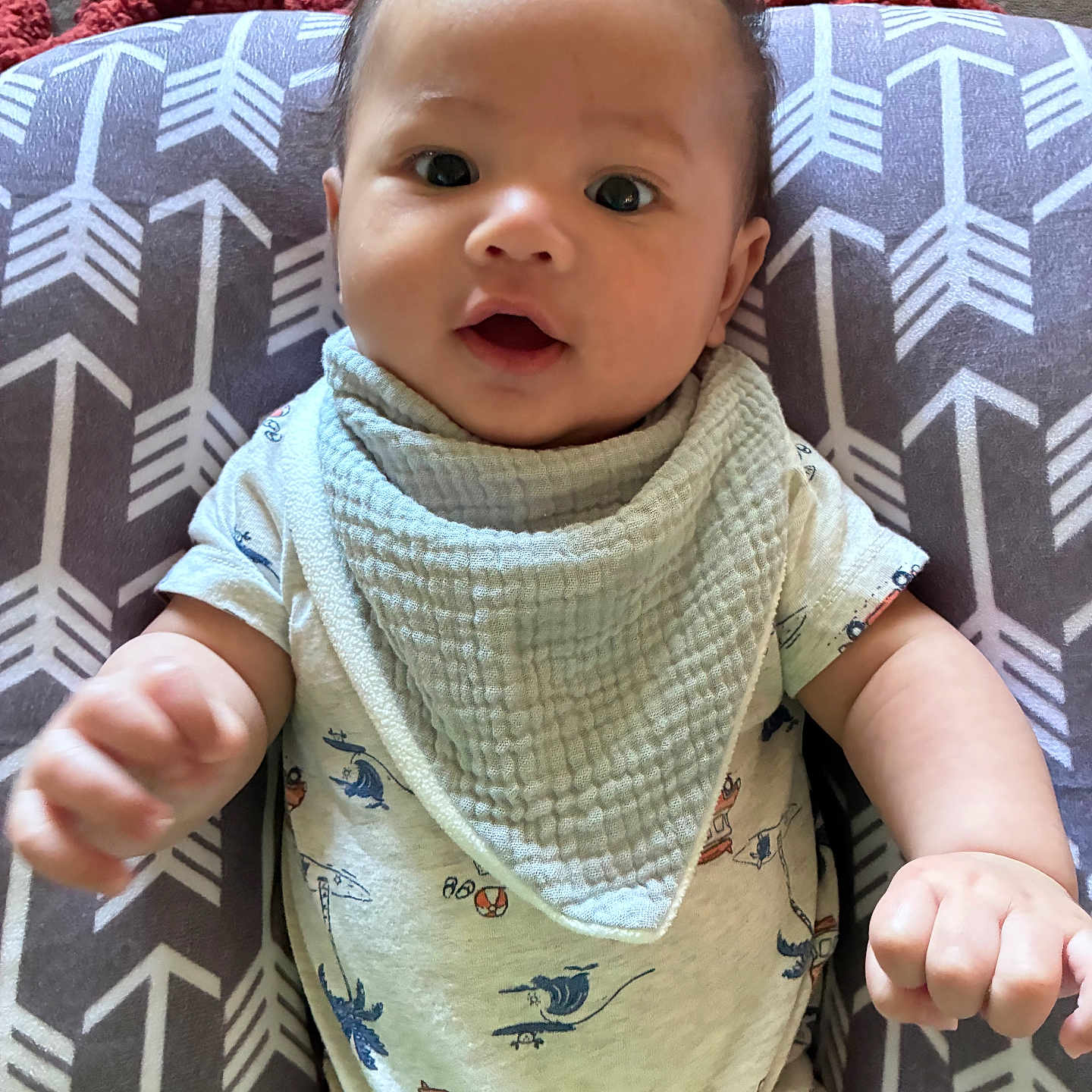 Kai is registered to the contest to win money with this photo: baby, infant, child, face, eyes, hair, bib, onesie, pattern, cushion, fabric, hand, fist, sitting, indoor, curious, cute, young, portrait, clothing