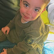Aylan participe au concours pour gagner de l'argent avec cette photo : child, toddler, smile, face, clothing, sneakers, shoe, sitting, bed, blanket, indoor, person, cute, young_child, portrait, casual_wear, hand, looking_up, happy, cozy