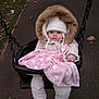 baby, child, swing, blanket, pink_blanket, fur_hood, white_hat, winter_clothing, outdoor, playground, fall_leaves, pavement, cold_weather, cute, infant, seated, person, face, footwear, cozy