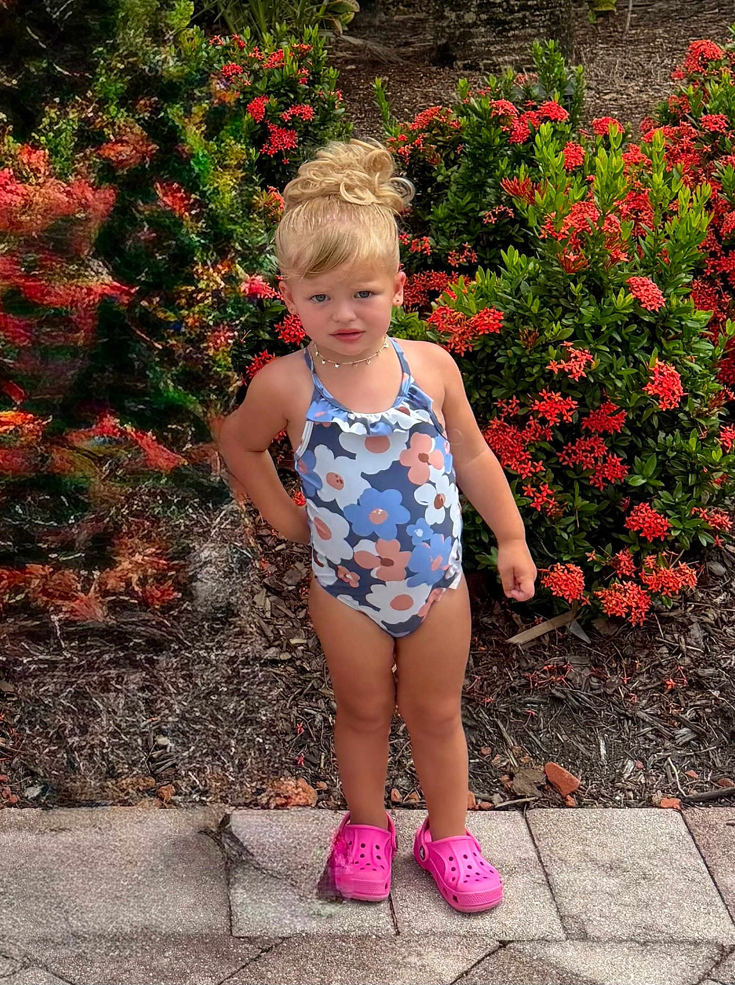 Margaux joined the competition — help win amazing prizes! child, girl, swimsuit, pink_crocs, flower_pattern, standing, outdoor, plants, greenery, red_flowers, sidewalk, hair_bun, summer, confident, nature, garden, young_child, casual, daylight, portrait