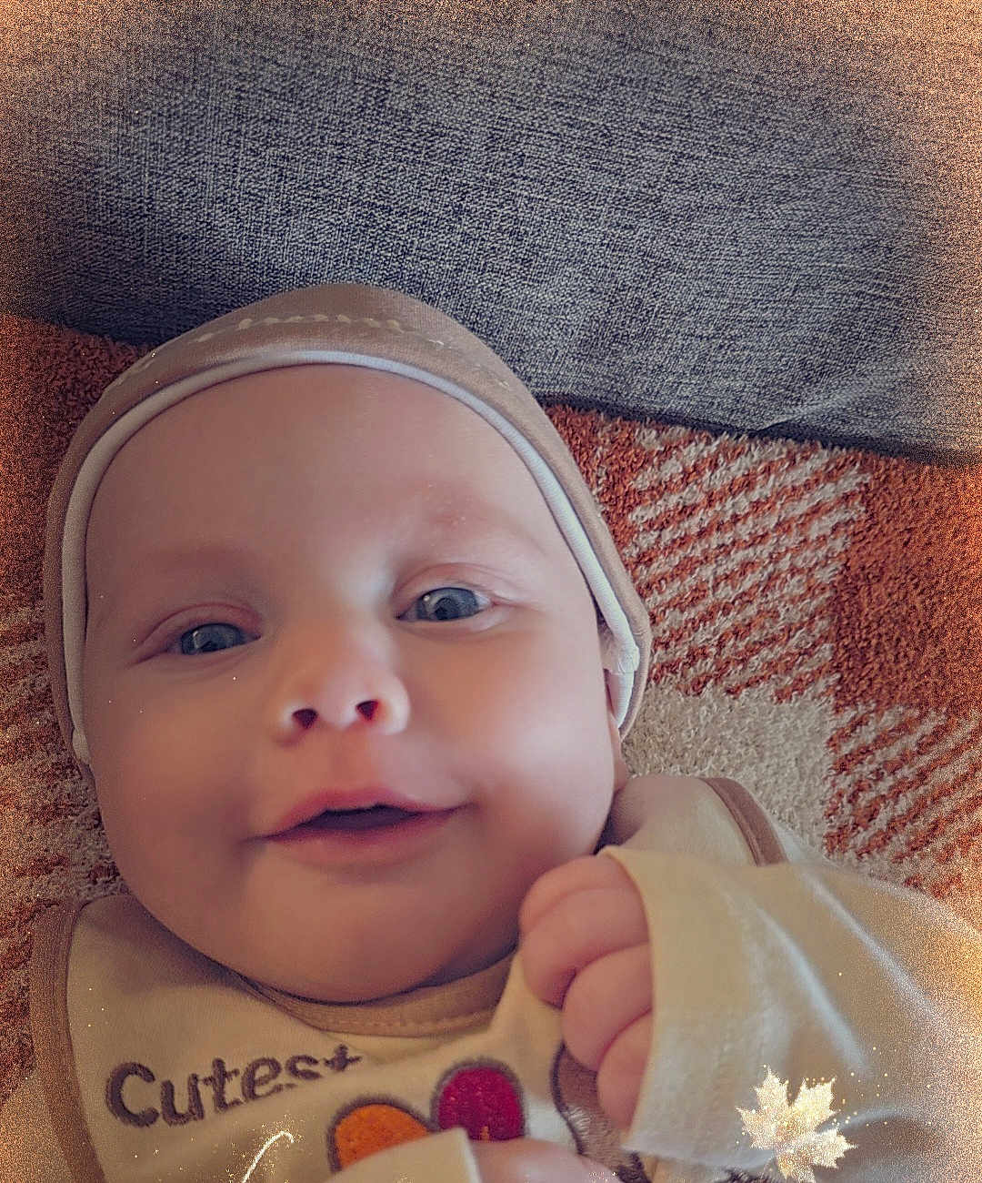 Jensen joined the competition — help win amazing prizes! baby, infant, face, smile, hat, clothing, blanket, closeup, cute, child, person, portrait, lying_down, happy, skin, headwear, warm_colors, soft_texture, indoors, newborn