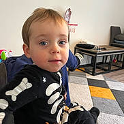 Noah participe au concours pour gagner de l'argent avec cette photo : toddler, child, boy, indoor, couch, skeleton_outfit, carpet, basketball_hoop, toy, face, blue_eyes, hair, clothing, furniture, floor, person, home, casual, playful, portrait
