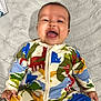 Ruhan Aditiyaa is registered to the contest to win money with this photo: baby, infant, smile, laughing, onesie, dinosaur_print, colorful_clothing, blanket, soft_texture, portrait, face, hands, small_fingers, sitting, indoors, bald_head, cheeks, closeup, playful, happy