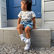 Vaiana a rejoint le concours — aidez-le/la à gagner de superbes lots ! toddler, child, sitting, blue_door, stone_steps, denim_shorts, white_sneakers, white_socks, gravel, outdoor, curious, side_profile, short_hair, casual_clothing, daylight, young_child, front_entrance, building_wall, footwear, portrait