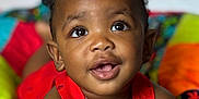 Zakai joined the competition — help win amazing prizes! baby, child, infant, red_clothing, colorful_quilt, bottle, smiling, curious, lying_down, close_up, face, bright_eyes, indoor, soft_light, happy, cute, skin, person, portrait, young_child