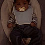 Mekhi joined the competition — help win amazing prizes! baby, baby_seat, bib, child, clothing, cozy, cushion, cute, dark_lighting, hat, indoor, infant, knitwear, pacifier, person, portrait, relaxed, seat, sleepwear, young_child