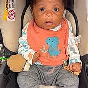 Mekhi joined the competition — help win amazing prizes! baby, bib, blue_socks, car_seat, child, clothing, comfort, cozy, cute, dinosaur, expression, face, indoor, infant, pacifier, person, portrait, sitting, teddy_bear, young