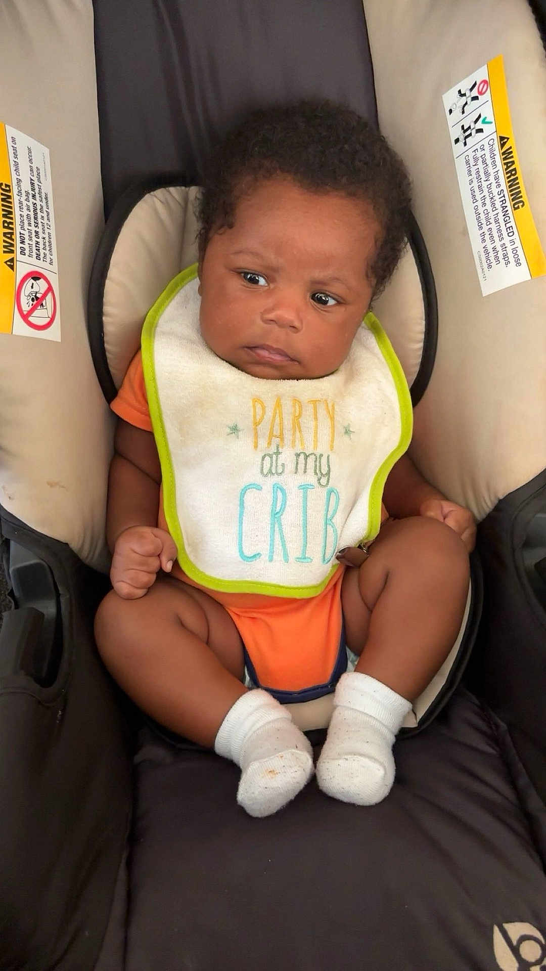 Mekhi is registered to the contest to win money with this photo: baby, infant, car_seat, bib, orange_clothing, socks, child, seat, cute, young, portrait, indoor, face, expression, skin, hair, person, clothing, warning_label, sitting