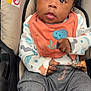 Mekhi is registered to the contest to win money with this photo: baby, bib, blue_socks, car_seat, casual_wear, child, clothing, comfortable, curly_hair, cute, dinosaur_print, expression, gray_pants, hands, indoors, infant, looking_up, portrait, seatbelt, young_child