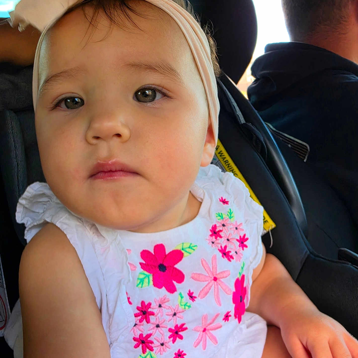 Olivia is registered to the contest to win money with this photo: toddler, child, baby, headband, bow, white_dress, floral_embroidery, car_seat, car_interior, person, face, hand, seatbelt, driver, window, daylight, cute, portrait, young_child, sitting