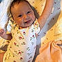 Mabel is registered to the contest to win money with this photo: baby, smiling, waving, onesie, floral_pattern, blanket, plush_toy, lying_down, happy, face, infant, child, bed, sheet, cheerful, cute, skin, arm, person, indoors