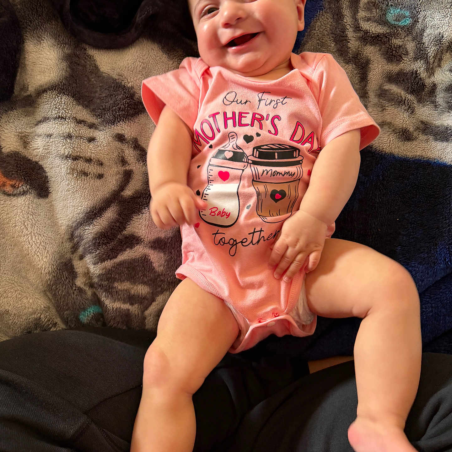 Delilah joined the competition — help win amazing prizes! baby, infant, smile, pink_onesie, mothers_day, blanket, pattern, happy, cute, child, face, legs, arms, skin, lying_down, indoors, person, portrait, newborn, clothing