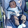 baby, child, infant, stroller, outdoor, grass, sunlight, portrait, face, eyes, serious_expression, white_shirt, brown_pants, white_socks, seatbelt, harness, carriage, park, sitting, close_up