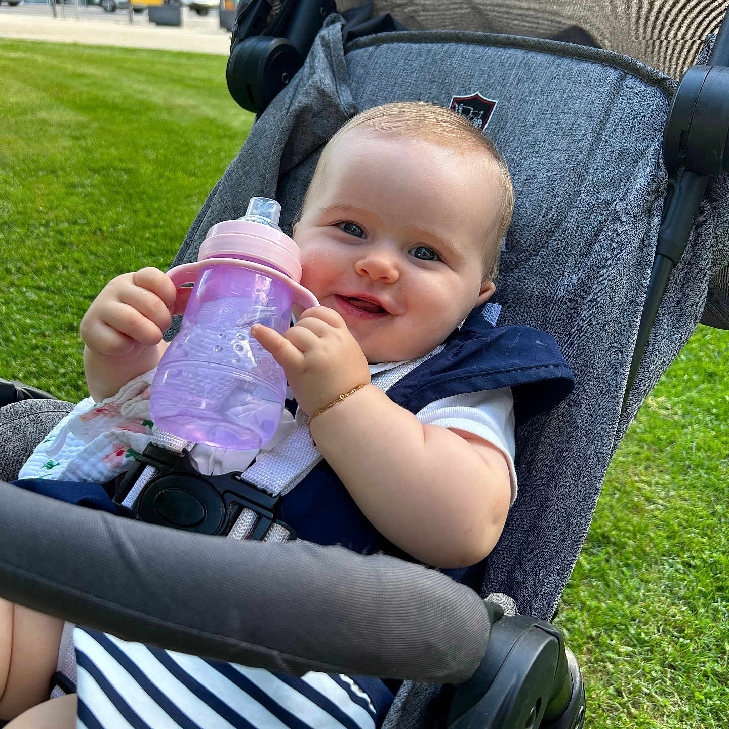 Nina-Rose participe au concours pour gagner de l'argent avec cette photo : baby, bracelet, cheeks, child, daytime, fabric, grass, hand, happy, infant, outdoor, person, seatbelt, sippy_cup, smiling, striped_clothing, stroller, sunlight, urban, wheel