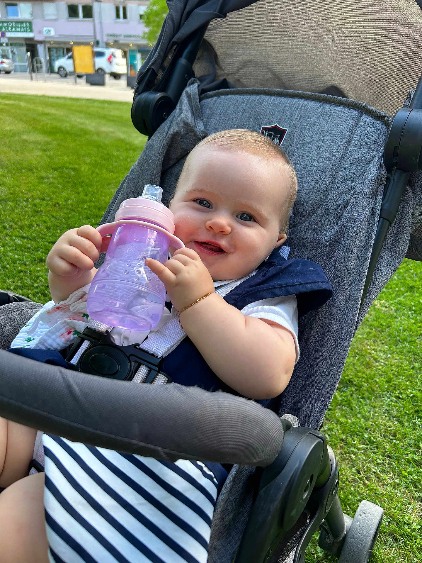Nina-Rose participe au concours pour gagner de l'argent avec cette photo : baby, child, stroller, outdoor, grass, smiling, sippy_cup, striped_clothing, happy, person, infant, seatbelt, sunlight, cheeks, hand, bracelet, urban, wheel, fabric, daytime