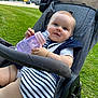 baby, stroller, sippy_cup, grass, outdoor, child, blue_eyes, striped_clothing, navy_blue, bracelet, cute, sunny, daytime, park, seatbelt, wheels, person, infant, happy, portrait