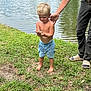 Weston is registered to the contest to win money with this photo: child, toddler, barefoot, fish, pond, grass, water, shorts, shirtless, adult_hand, outdoor, nature, summer, person, fishing, curious, greenery, daylight, recreation, family