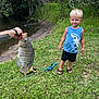 Weston joined the competition — help win amazing prizes! child, boy, blond_hair, blue_shirt, shark_print, shorts, sandals, grass, riverbank, trees, fishing_rod, fish, fishing, outdoor, nature, tattoo, hand, summer, daytime, water