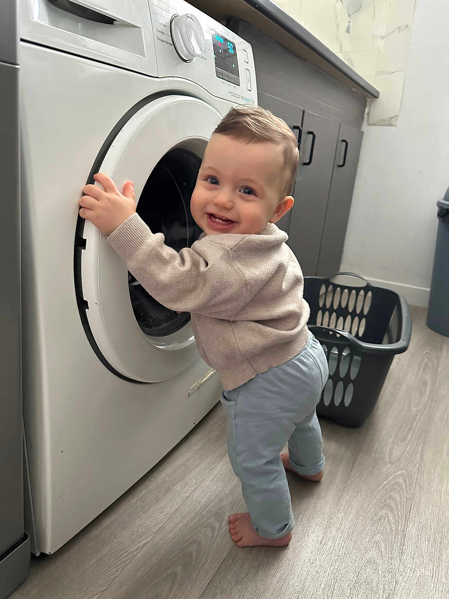 Lorenzo a rejoint le concours — aidez-le/la à gagner de superbes lots ! toddler, child, washing_machine, laundry_basket, barefoot, smiling, indoor, flooring, cabinet, clothing, sweater, pants, home, appliance, household, cute, standing, face, happy, person