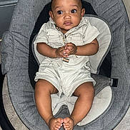 Denzel joined the competition — help win amazing prizes! baby, infant, child, baby_rocker, gray_cushion, romper, clothing, hands, feet, floor, indoor, curious_expression, wide_eyes, black_hair, person, sitting, seat, baby_seat, floor_tile, cute