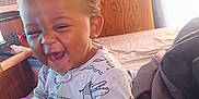 Christopher is registered to the contest to win money with this photo: baby, child, pajamas, toy, purple_toy, bed, bedroom, wood_paneling, window, curtain, smile, laughing, happy, indoor, person, clothing, cute, infant, sleepwear, cozy