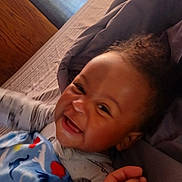 Christopher is registered to the contest to win money with this photo: baby, smiling, blanket, bed, pillow, child, happy, indoor, person, cute, cozy, infant, face, hand, clothing, sleepwear, portrait, lying_down, expression, comfort